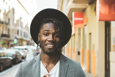 Close-up portrait of young man with braided hair wearing hat in city