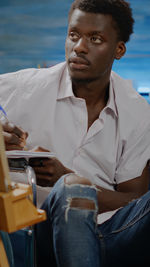 Young man looking away while sitting outdoors