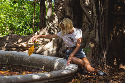 Woman throwing dry leaf in pond against tree at back yard