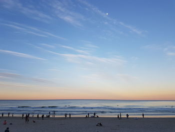 People at beach against sky during sunset