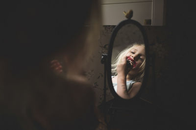 Girl applying lipstick while looking in mirror at home