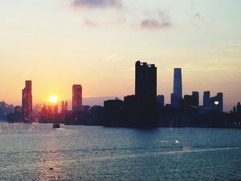 Sea by buildings against sky during sunset