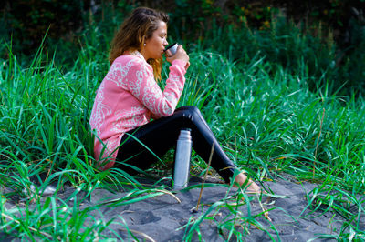 Full length of woman drinking water while sitting on grass