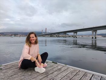 Woman sitting on bridge over pier against sky