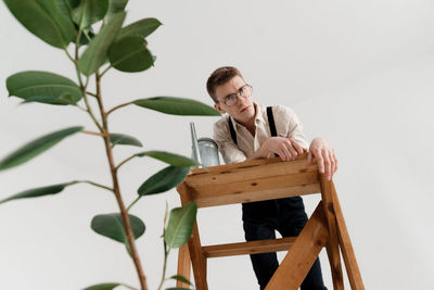 Low angle portrait of man standing on ladder against white background