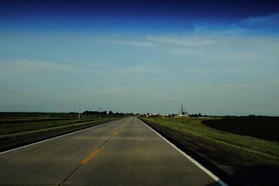 Road passing through field against sky