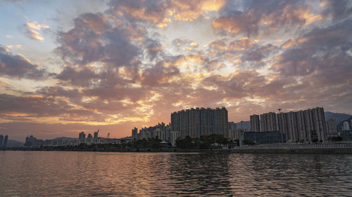 Scenic view of river by buildings against sky during sunset