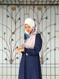 Portrait of young woman standing against wall