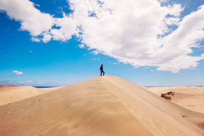 Man on sand dune in desert against sky