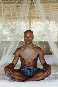 Smiling shirtless man sitting on bed