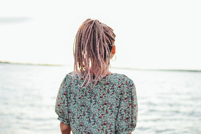 Rear view of young woman standing at beach against sky