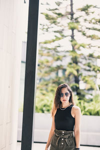 Portrait of young woman standing against window