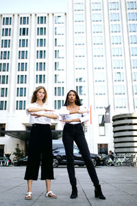 Low angle portrait of female friends gesturing equal sign while standing against building in city