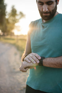 Young male athlete looking at smart watch while standing park