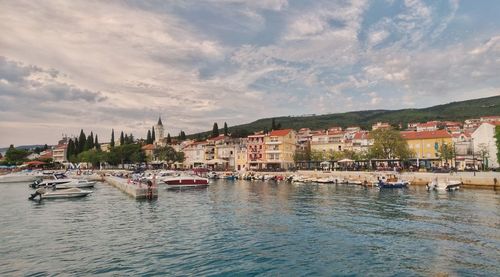 Sailboats moored on river by buildings against sky