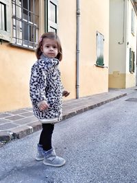 Portrait of cute girl standing on street by buildings in city