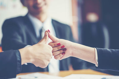 Close-up of business colleagues gesturing thumbs up in office