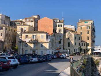 Cars on street by buildings against clear blue sky