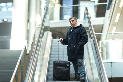 Portrait of mature man with suitcase standing on escalator at station