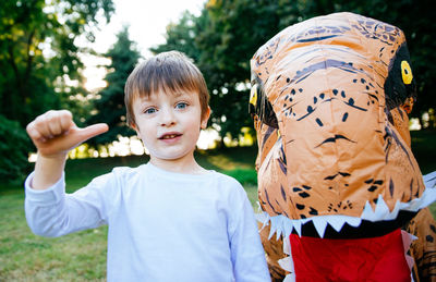 Portrait of cute boy with person wearing dinosaur costume in park