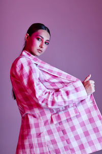 Portrait of young woman standing against pink background