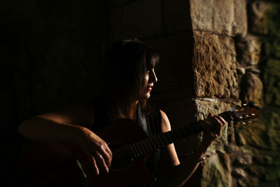 Woman playing guitar by stone wall