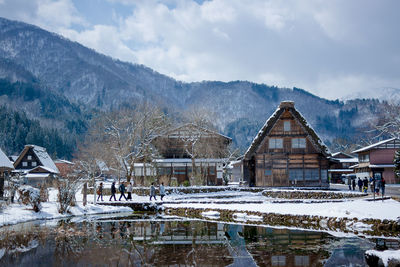 Houses by lake against sky during winter