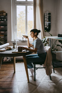 Side view of female freelancer talking on speaker while sitting on chair at home office