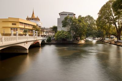 Arch bridge over river amidst buildings against sky