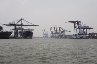 Cranes at harbor against sky