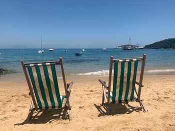 Deck chairs on beach against clear sky