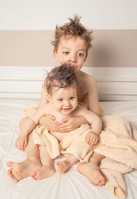 Siblings with towel on bed at home