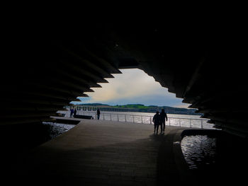 Silhouette people walking on bridge against sky