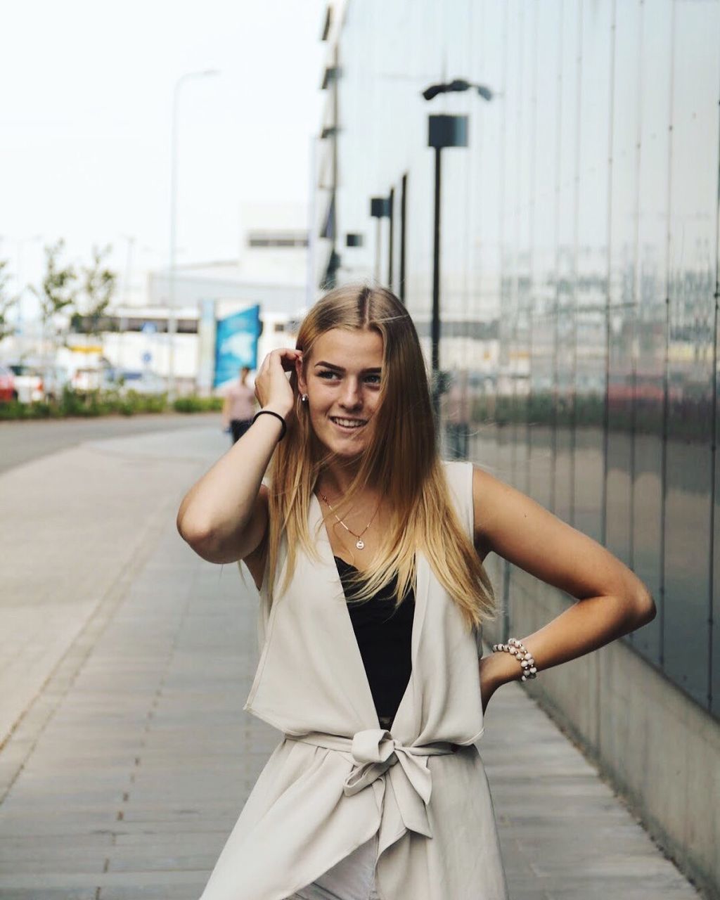 PORTRAIT OF A SMILING YOUNG WOMAN STANDING AGAINST THE WALL