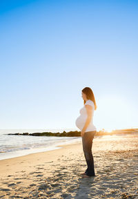 Full length of young woman standing at beach against clear sky