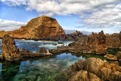 Rock formations on sea against cloudy sky