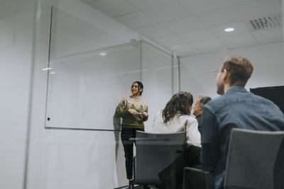 Businesswoman explaining strategy while standing by whiteboard near colleagues in board room