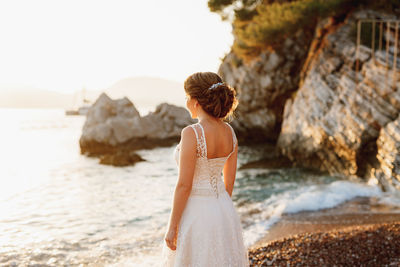 Rear view of woman standing on rock at beach