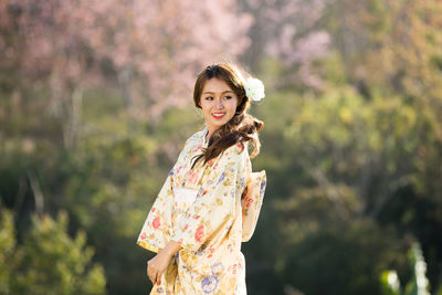 Portrait of smiling young woman standing against plants