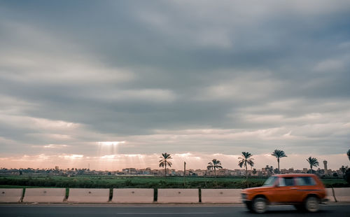 Cars on road by field against sky during sunset