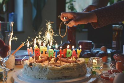 Cropped hand igniting candle on birthday cake at home