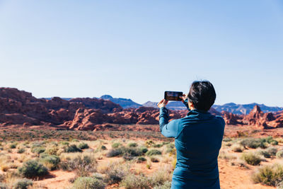 Rear view of person photographing on smart phone against sky