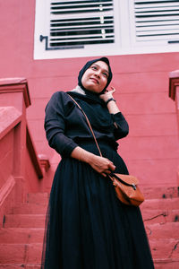 Portrait of smiling young woman standing against wall