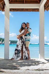 Young couple embrace under the shade of a gazebo while standing at the beach