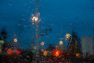 Illuminated lights seen through wet car window during rainy season