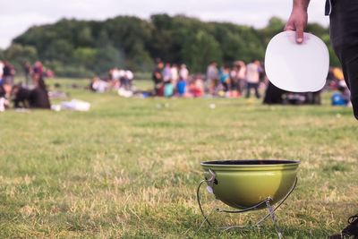 Cropped image of man holding plate over barbecue grill on field