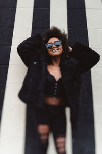 Portrait of woman in sunglasses and fur coat against wall