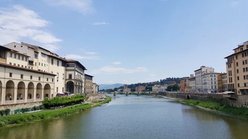 Arch bridge over river amidst buildings in city against sky