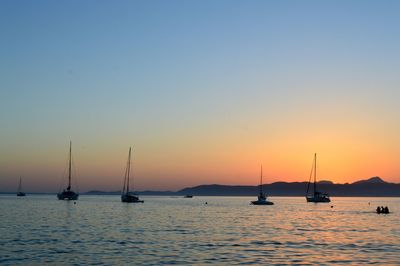 Sailboats moored in sea against sky during sunset