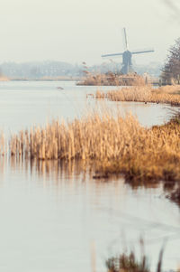 Traditional windmill by lake against clear sky